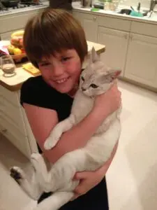 A boy holding a cat in his arms.